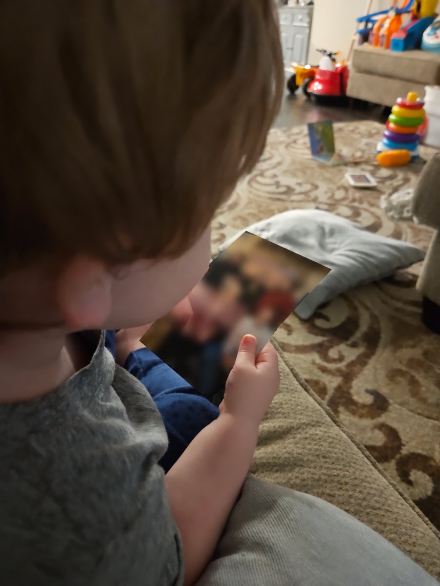 A small child, seen from behind, holding a printed family photograph