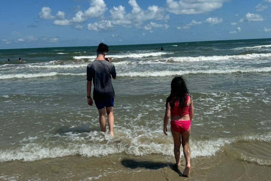 Two children, seen from behind, wading into the surf on a bright day
