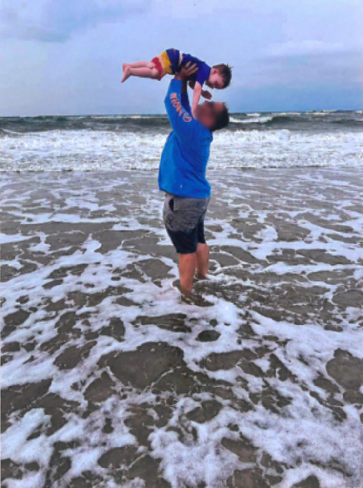 A father lifting a small child high above his head at the edge of the sea